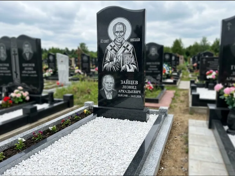 Памятник с гравировкой иконы: стела с крестообразным навершием — икона в резной рамке-киоте, газон без ограды, стриженая трава, работа «Раевская» в Москве