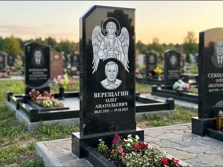 Памятник с гравировкой иконы: стела с резным навершием и нимбом в золоте — гравировка образа Спасителя, высокие разросшиеся туи полукругом, работа «Мельникова» в Москве
