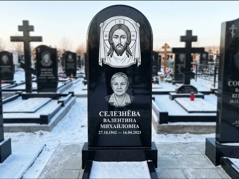 Памятник с гравировкой иконы: небольшая скромная одиночная стела с именной иконой — золочёный нимб на образе, аккуратный участок с газоном, работа «Ковалёв» в Москве