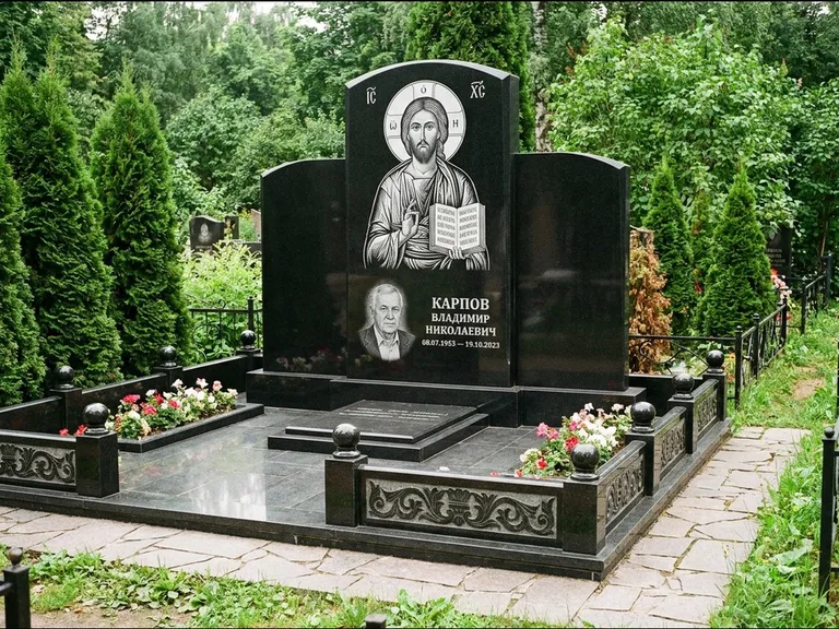 Памятник с гравировкой иконы: широкая панорамная стела с золочёным нимбом — гравировка образа Матроны Московской, цветник с белыми хризантемами, работа «Мельникова» в Москве
