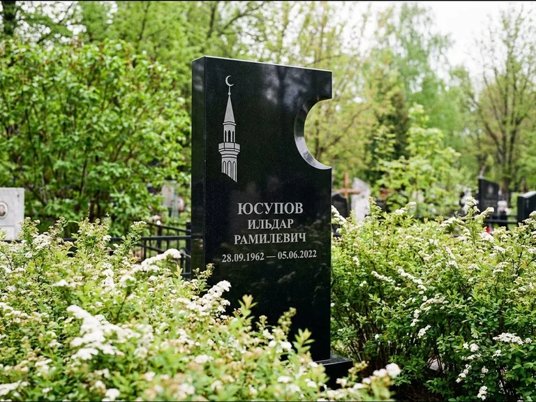 Мусульманский памятник с гравировкой мечети: стела с боковым вырезом в форме полумесяца — гравировка минарета с полумесяцем, низкие кусты спиреи в цвету, работа «Юсупов» в Москве